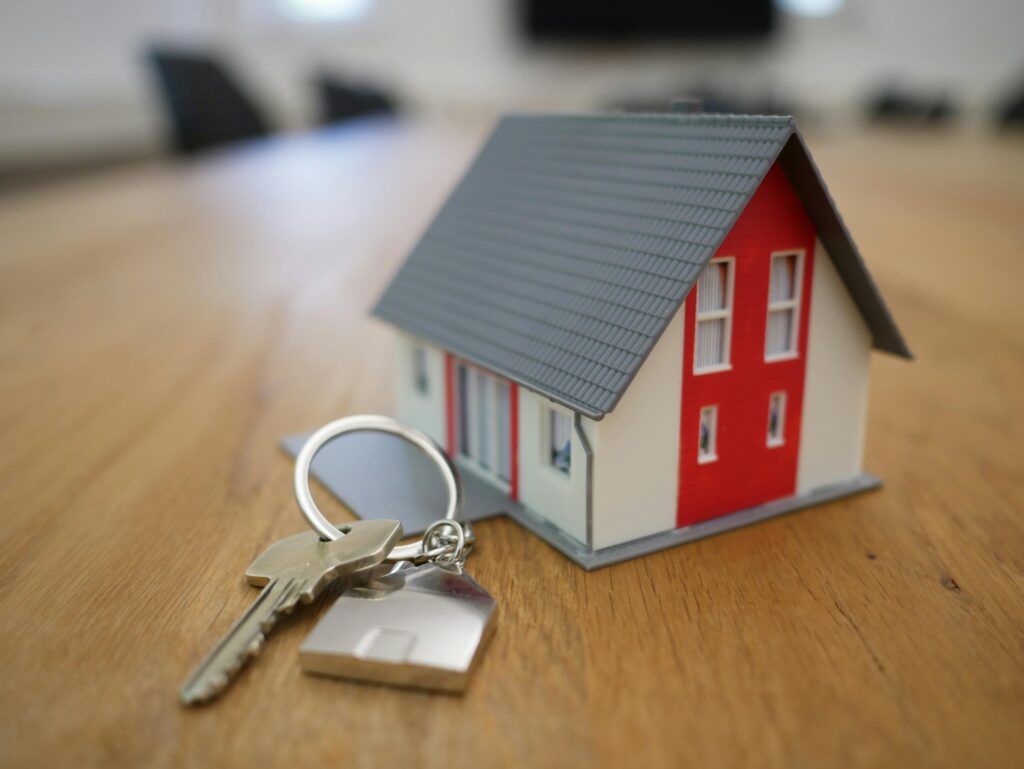 A small model of a home sat on a table with keys to a home resting on the table. 